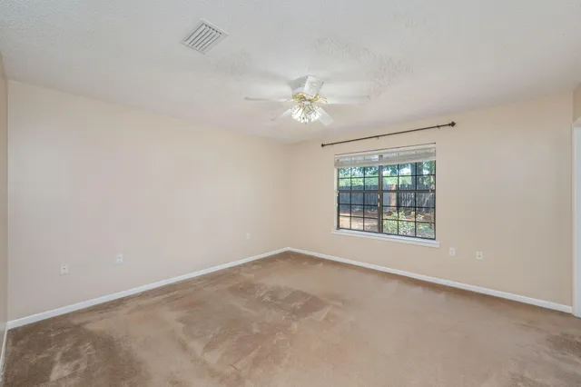 an empty room with chandelier fan and windows