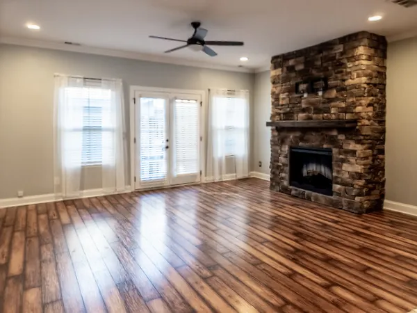 an empty room with wooden floor fireplace cabinet and windows