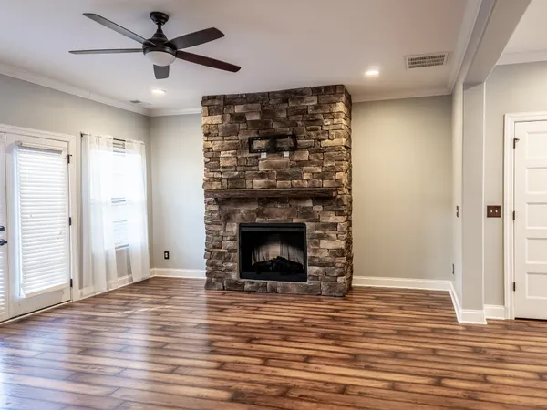 an empty room with wooden floor a ceiling fan a fireplace and windows
