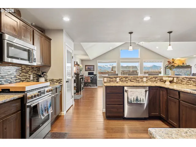 a kitchen with stainless steel appliances granite countertop a stove a sink dishwasher a refrigerator and white cabinets with wooden floor