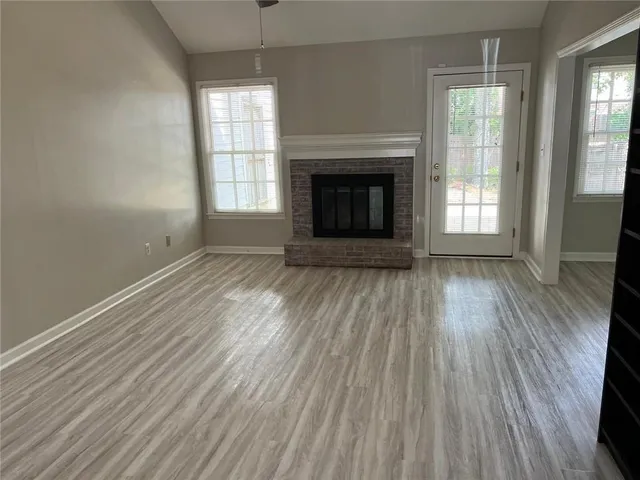 an empty room with wooden floor fireplace and windows