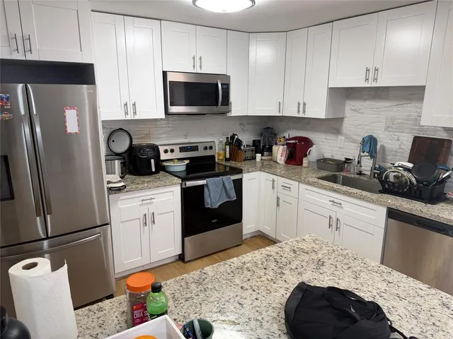 a kitchen with stainless steel appliances kitchen island granite countertop a sink dishwasher stove top oven and refrigerator with wooden cabinets