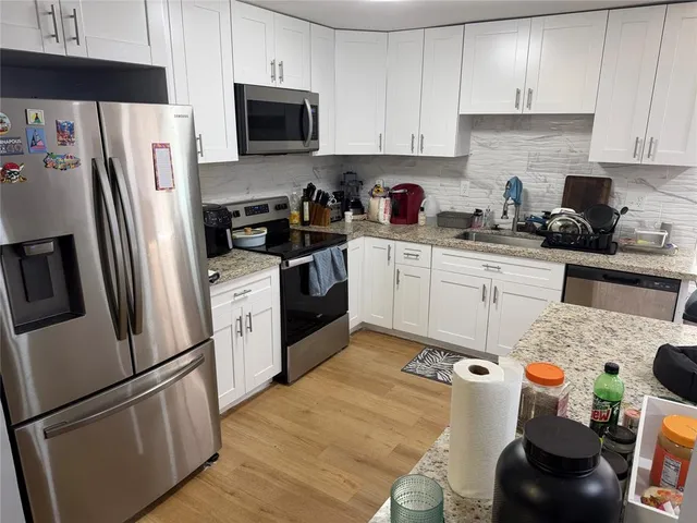 a kitchen with stainless steel appliances granite countertop a refrigerator stove a sink dishwasher and white cabinets