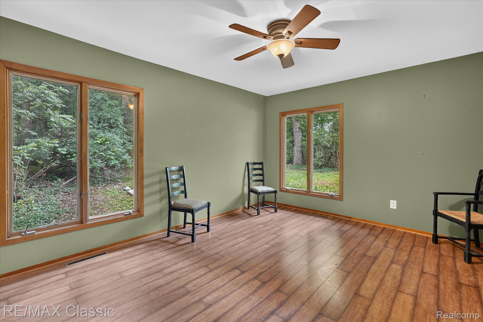 12189 Gage Road Holly, MI 48442 - Photo 23 of 69 Room featuring wood-finish flooring, two large windows with wood trim, a ceiling fan with light fixture, and light green wall paint