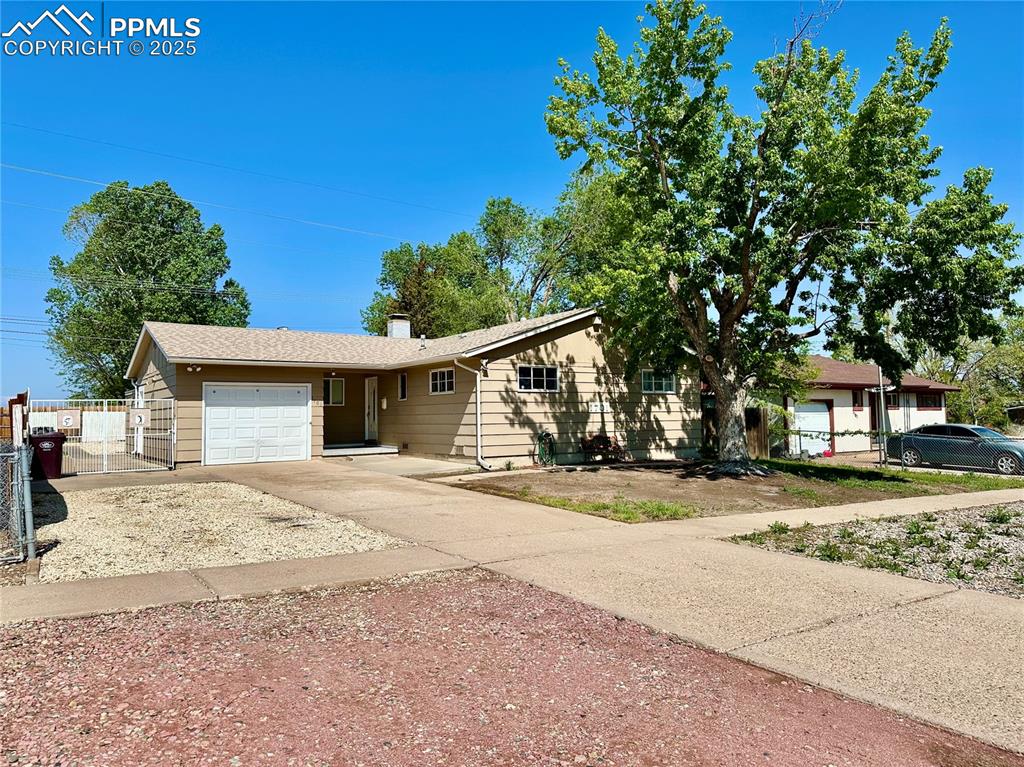 View of front facade with an attached garage, concrete driveway, a chimney, and fence