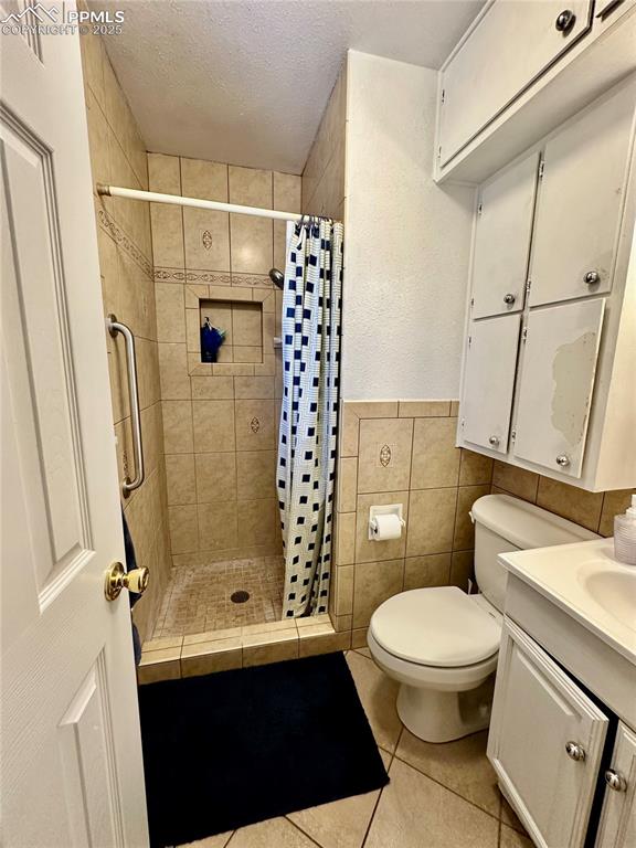 1701 Jerry Murphy Road Pueblo, CO 81001 - Photo 14 of 20 Bathroom featuring tile patterned flooring, a stall shower, a textured ceiling, toilet, and tile walls
