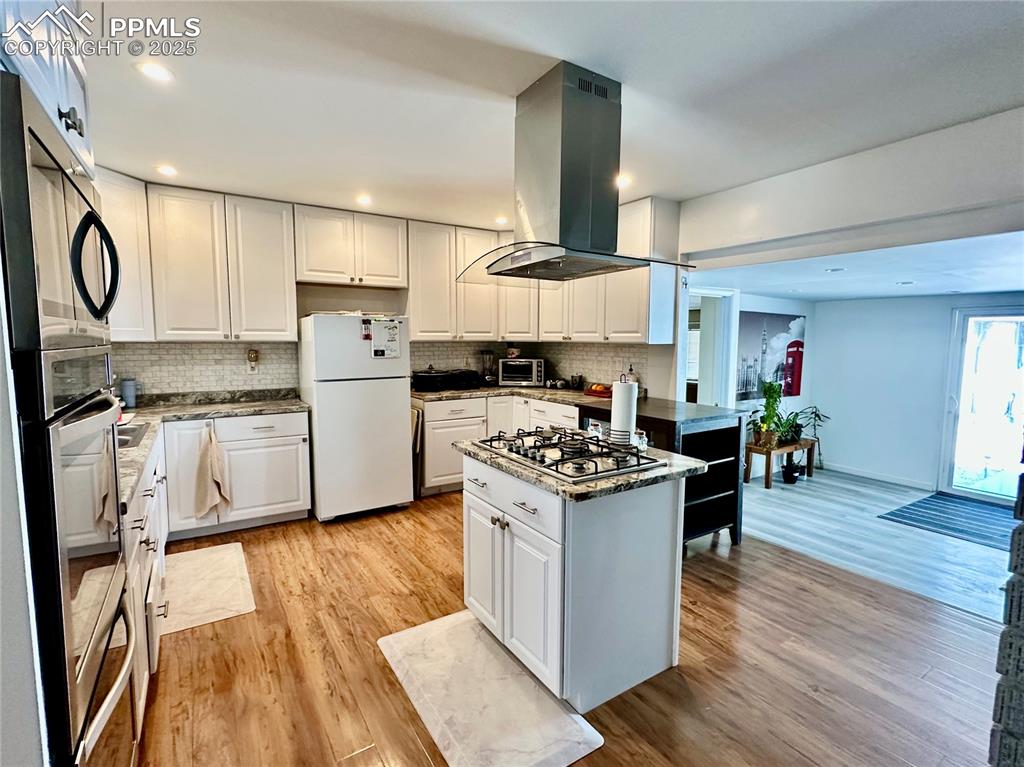 1701 Jerry Murphy Road Pueblo, CO 81001 - Photo 5 of 20 Kitchen featuring stainless steel appliances, island range hood, decorative backsplash, light wood-style flooring, and recessed lighting