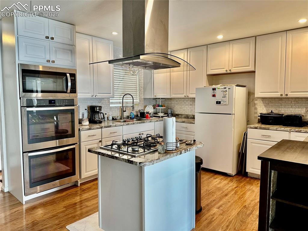 1701 Jerry Murphy Road Pueblo, CO 81001 - Photo 6 of 20 Kitchen with stainless steel appliances, island range hood, decorative backsplash, white cabinets, and recessed lighting