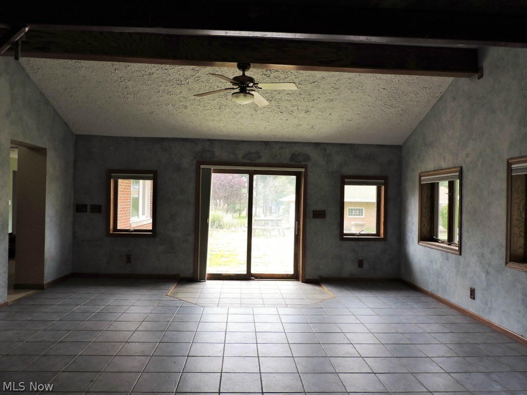 Great room with vaulted/beamed ceilings, radiant heat floors, wood burning stove with stone surround, and sliding door leading to the brick patio