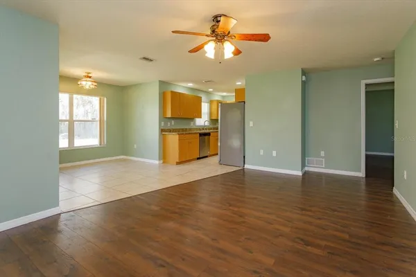 an empty room with wooden floor chandelier fan and windows