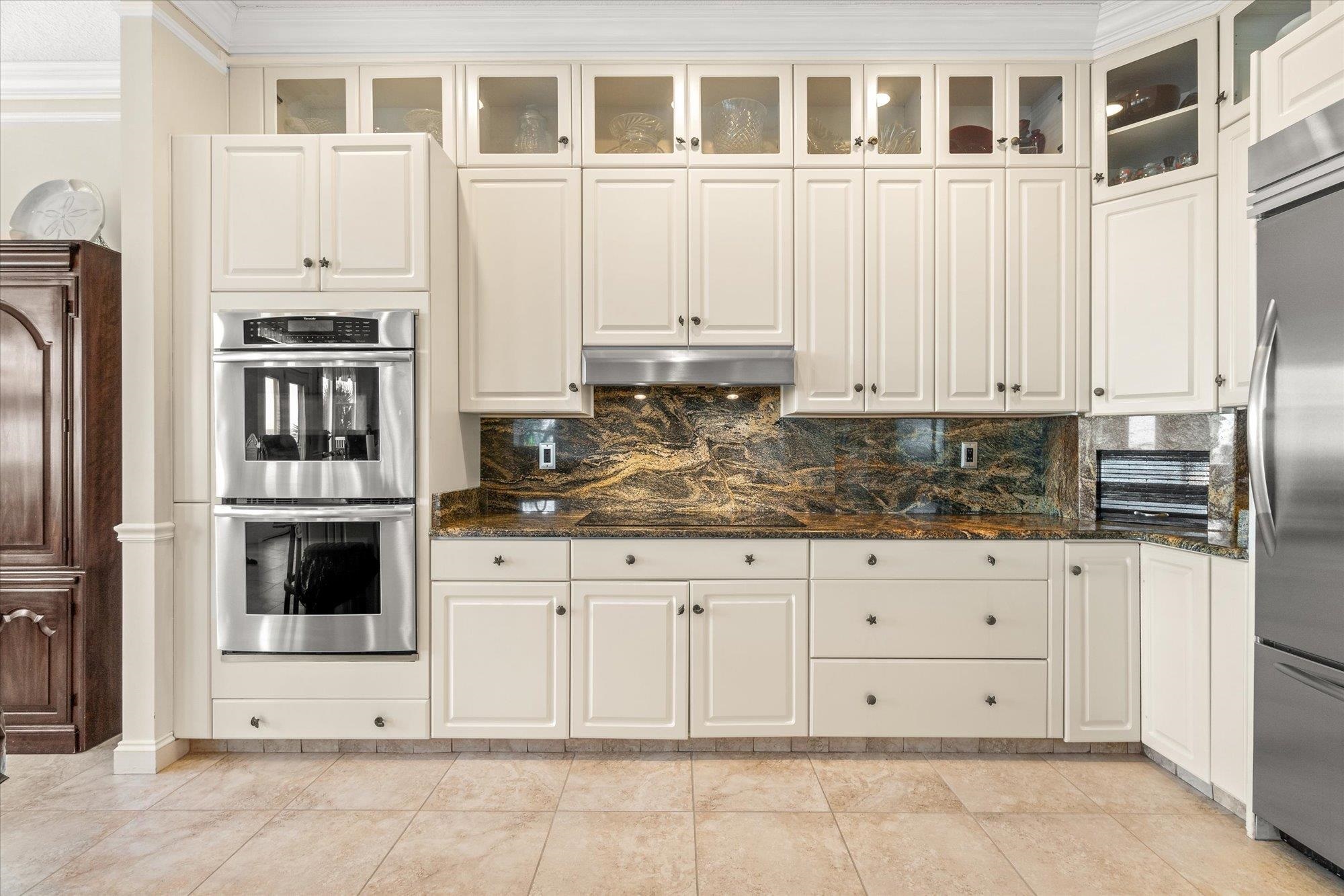5042 Atlantic View St. Augustine, FL 32080 - Photo 14 of 72 Kitchen with appliances with stainless steel finishes, crown molding, dark stone counters, decorative backsplash, and glass insert cabinets
