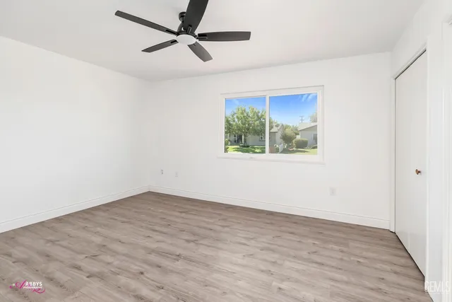 an empty room with wooden floor ceiling fan and windows