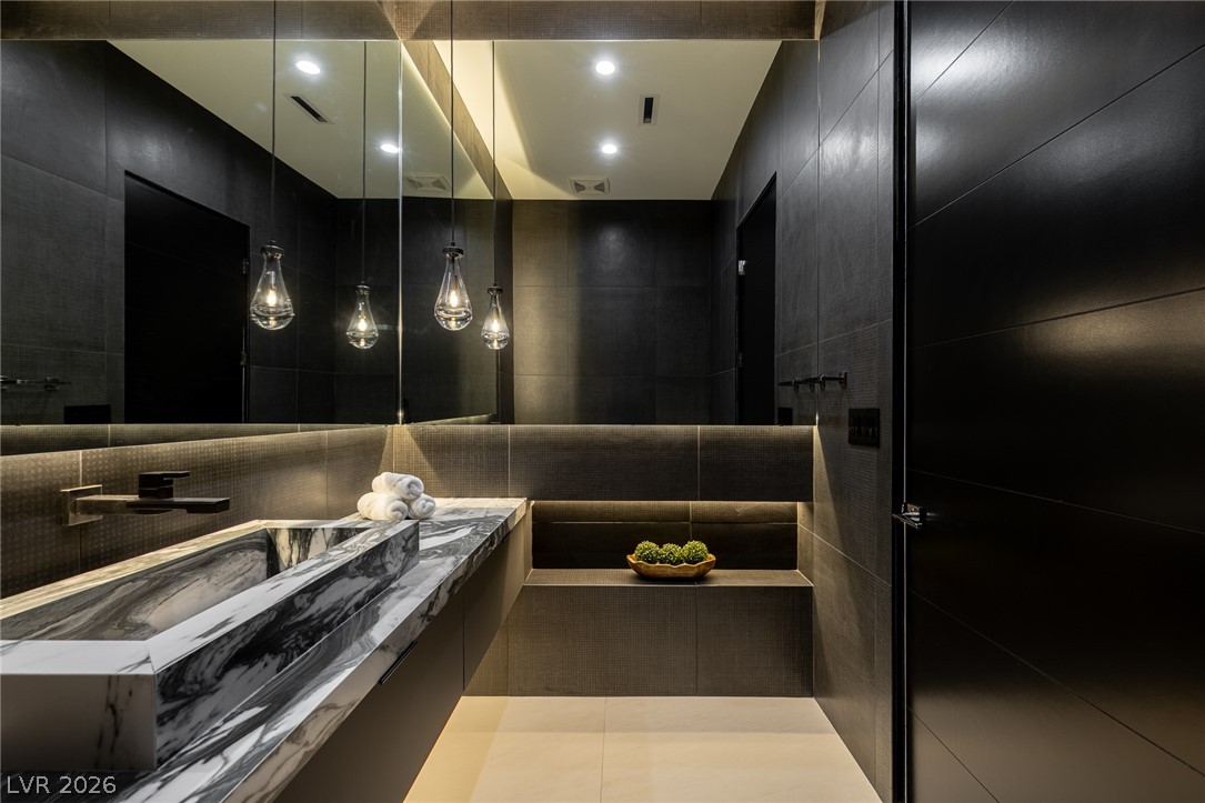 563 Grand Rim Drive Henderson, NV 89012 - Photo 30 of 70 A striking powder bathroom features a bold stone vanity, sleek dark tile walls, and modern pendant lighting.