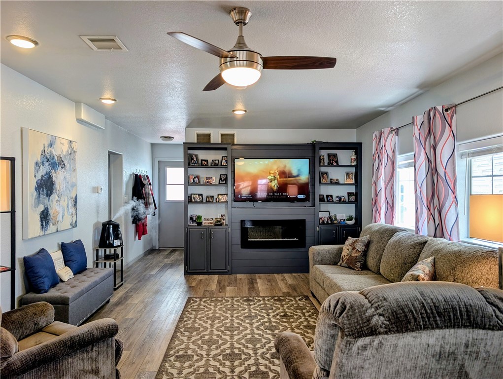 2000 Ramar Road, Unit 442 Bullhead City, AZ 86442 - Photo 12 of 28 Living room with a textured ceiling, ceiling fan, a glass covered fireplace, wood finished floors, and healthy amount of natural light