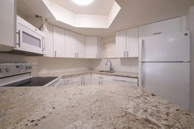 a kitchen with granite countertop a sink a refrigerator a stove and white cabinets