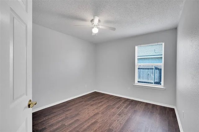an empty room with wooden floor chandelier fan and windows