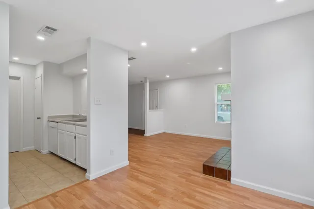 a view of an empty room with kitchen and wooden floor
