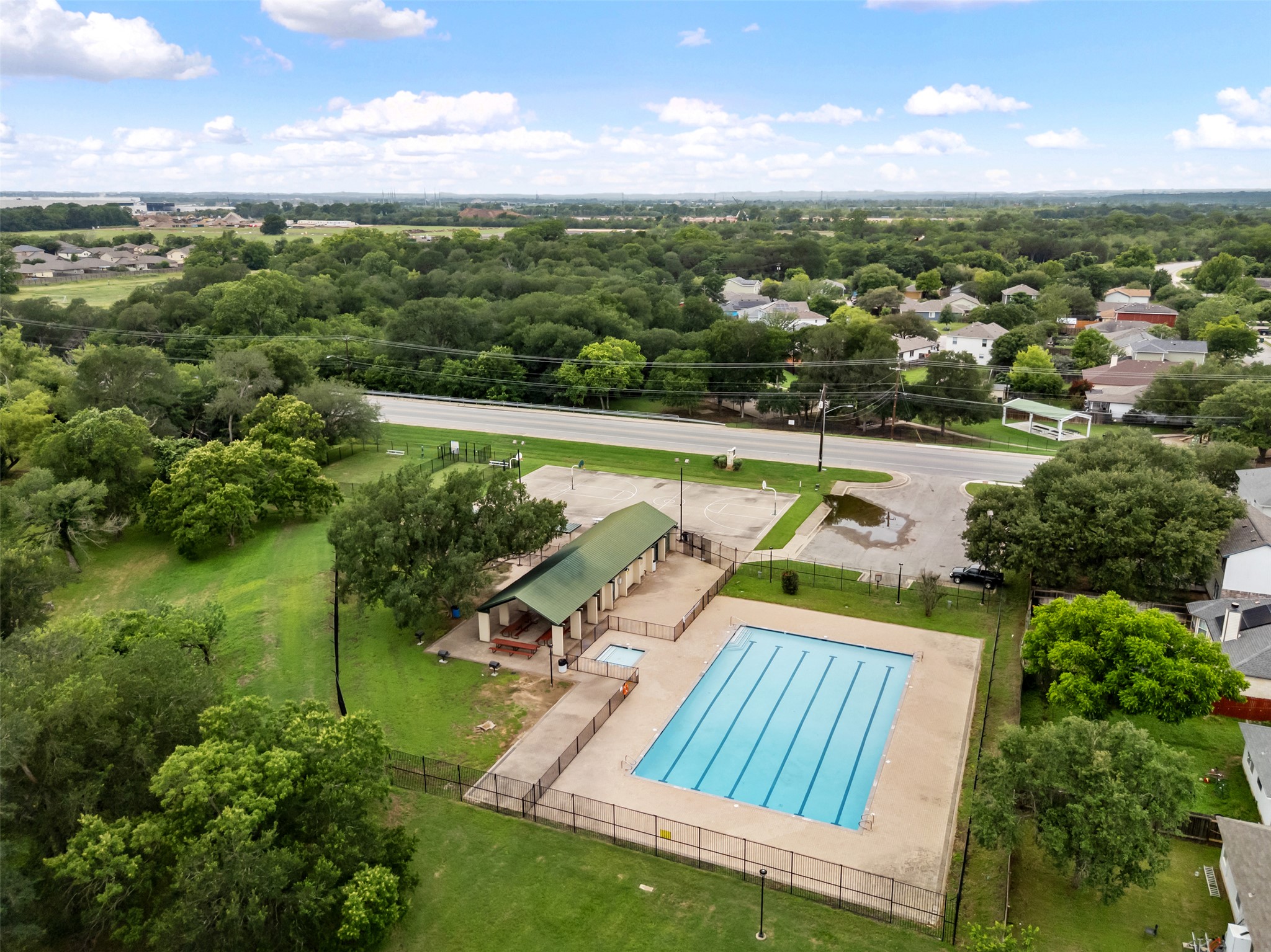 14900 Retha Pass Austin, TX 78725 - Photo 28 of 39 Recreational swimming pool with a surrounding concrete deck and black metal fencing, accompanied by a covered pavilion with a green roof