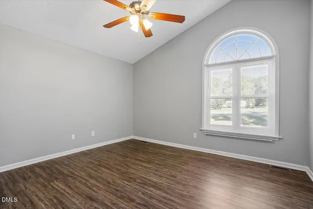 an empty room with wooden floor chandelier fan and windows