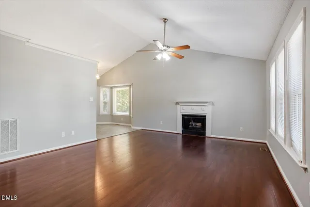 an empty room with wooden floor fireplace and windows