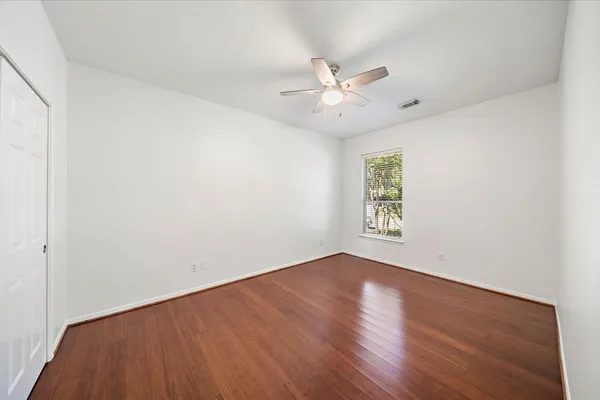 an empty room with wooden floor fan and windows