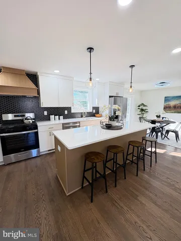 a kitchen with stainless steel appliances granite countertop a stove top oven a sink a dining table and chairs with wooden floor