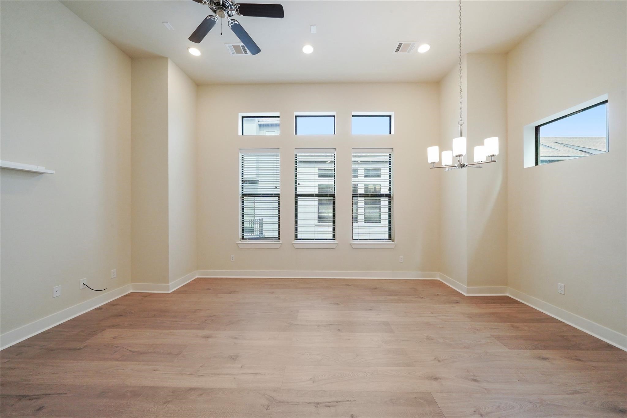 2616 Riverside Drive, Unit K Houston, TX 77004 - Photo 11 of 31 This spacious room features high ceilings with recessed lighting and a ceiling fan, large windows providing ample natural light, elegant light wood flooring, and a modern chandelier, creating a bright and inviting atmosphere.