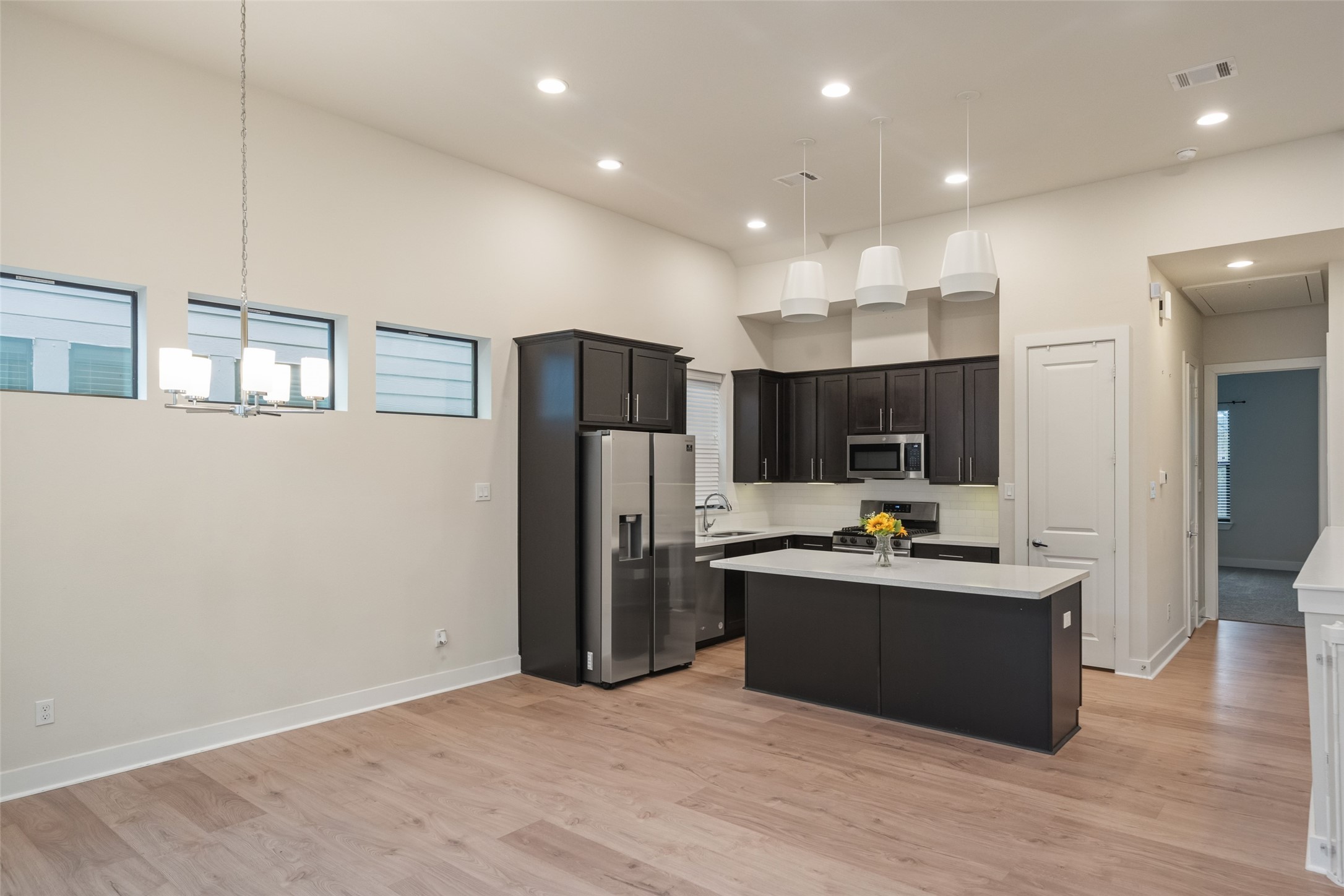 2616 Riverside Drive, Unit K Houston, TX 77004 - Photo 14 of 31 This photo showcases a modern kitchen with sleek dark cabinets, stainless steel appliances, and a central island. The open layout features light wood flooring and ample overhead lighting, complemented by three small windows and a contemporary ceiling fixture.