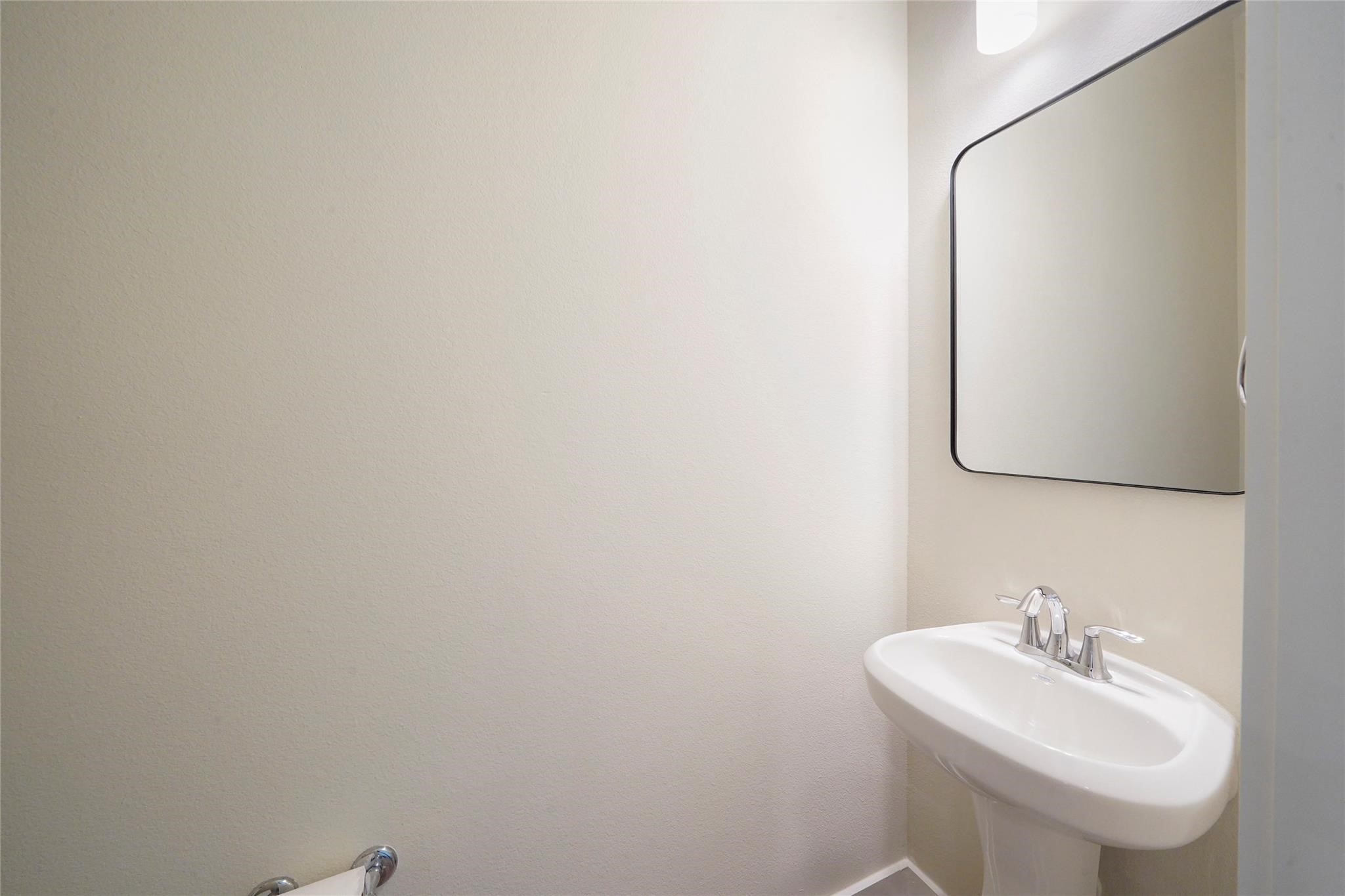 2616 Riverside Drive, Unit K Houston, TX 77004 - Photo 19 of 31 This is a small, modern bathroom featuring a sleek pedestal sink, a rectangular mirror with rounded edges, and bright, neutral walls.