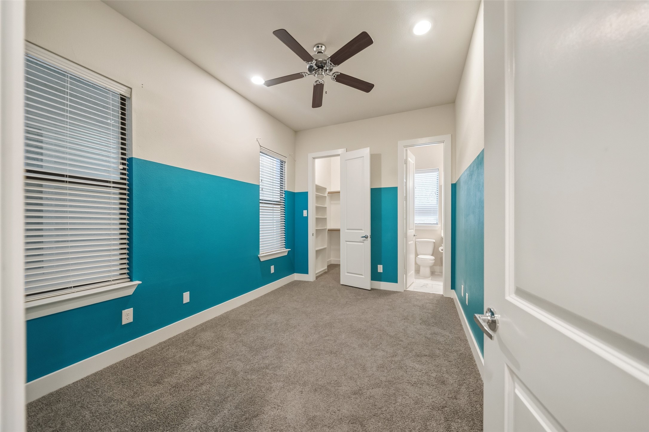 2616 Riverside Drive, Unit K Houston, TX 77004 - Photo 4 of 31 This is a bright, cozy bedroom with teal and white walls, carpeted flooring, and a ceiling fan. It features two windows with blinds, a closet, and an attached bathroom, creating a convenient and functional space.