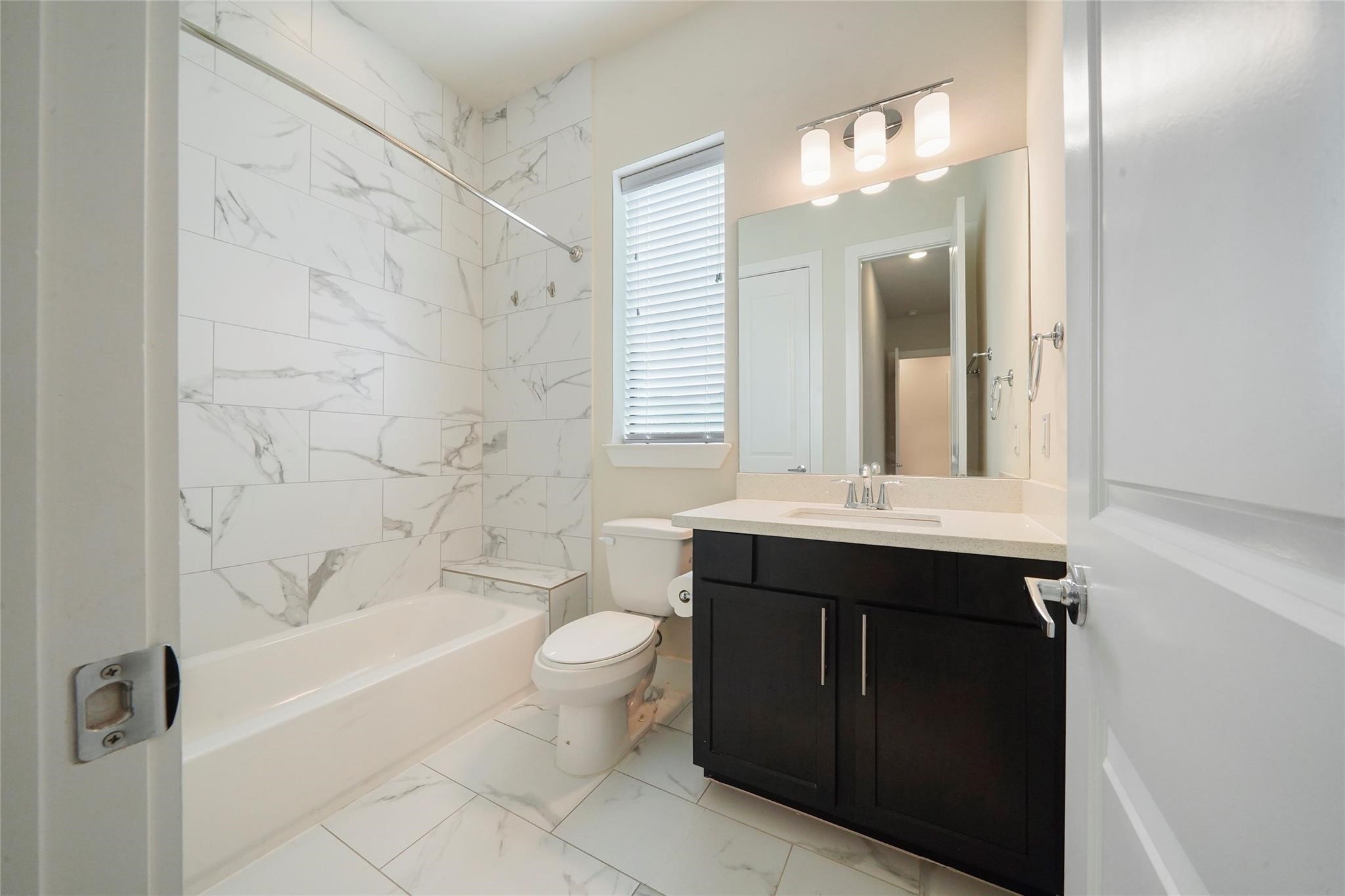 2616 Riverside Drive, Unit K Houston, TX 77004 - Photo 6 of 31 This bathroom features a sleek design with modern fixtures. It has a marble-tiled shower and tub, a large mirror above a dark wood vanity, and plenty of natural light from a window.