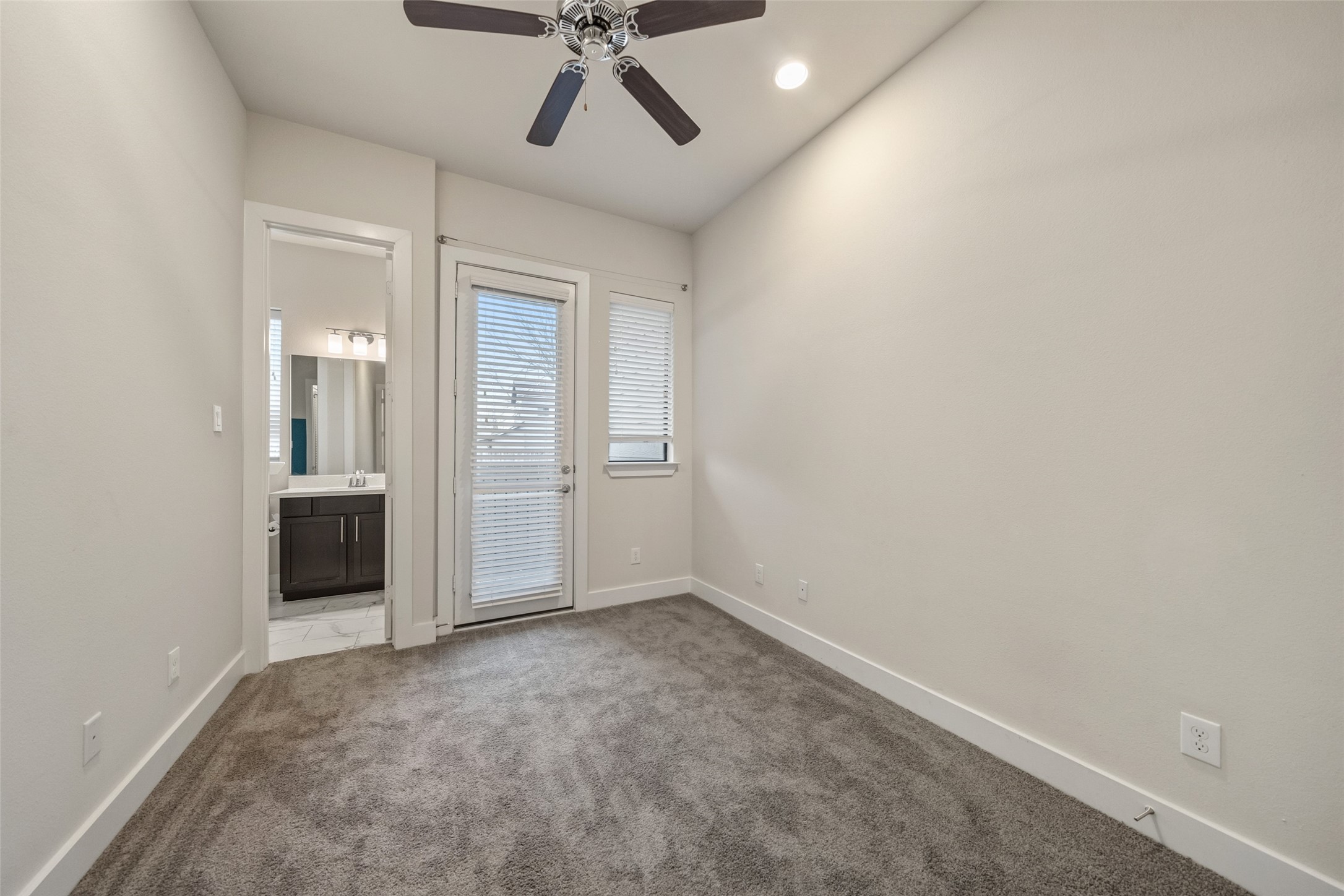 2616 Riverside Drive, Unit K Houston, TX 77004 - Photo 7 of 31 A cozy room with neutral walls and plush carpet, featuring a ceiling fan and access to a small outdoor area through a glass door. A doorway leads to a bathroom with modern fixtures. Ideal for a bedroom or office.