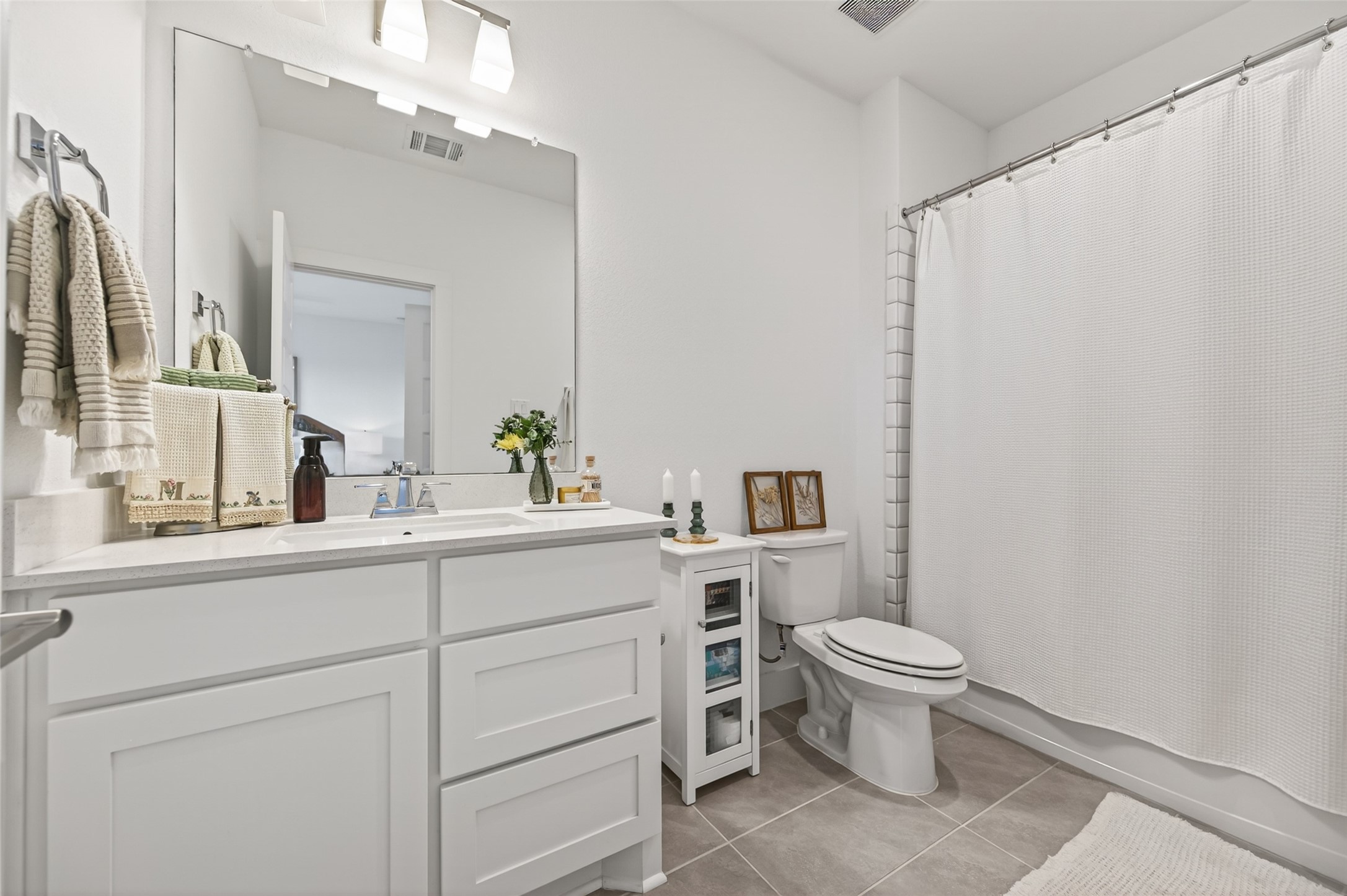 29612 Fulshear Lake Trace Fulshear, TX 77406 - Photo 46 of 48 This bright, modern bathroom features a large mirror, white cabinetry, and a clean, minimalist design. It includes a shower with a white curtain, a sink with stylish fixtures, and a small storage unit for added convenience.