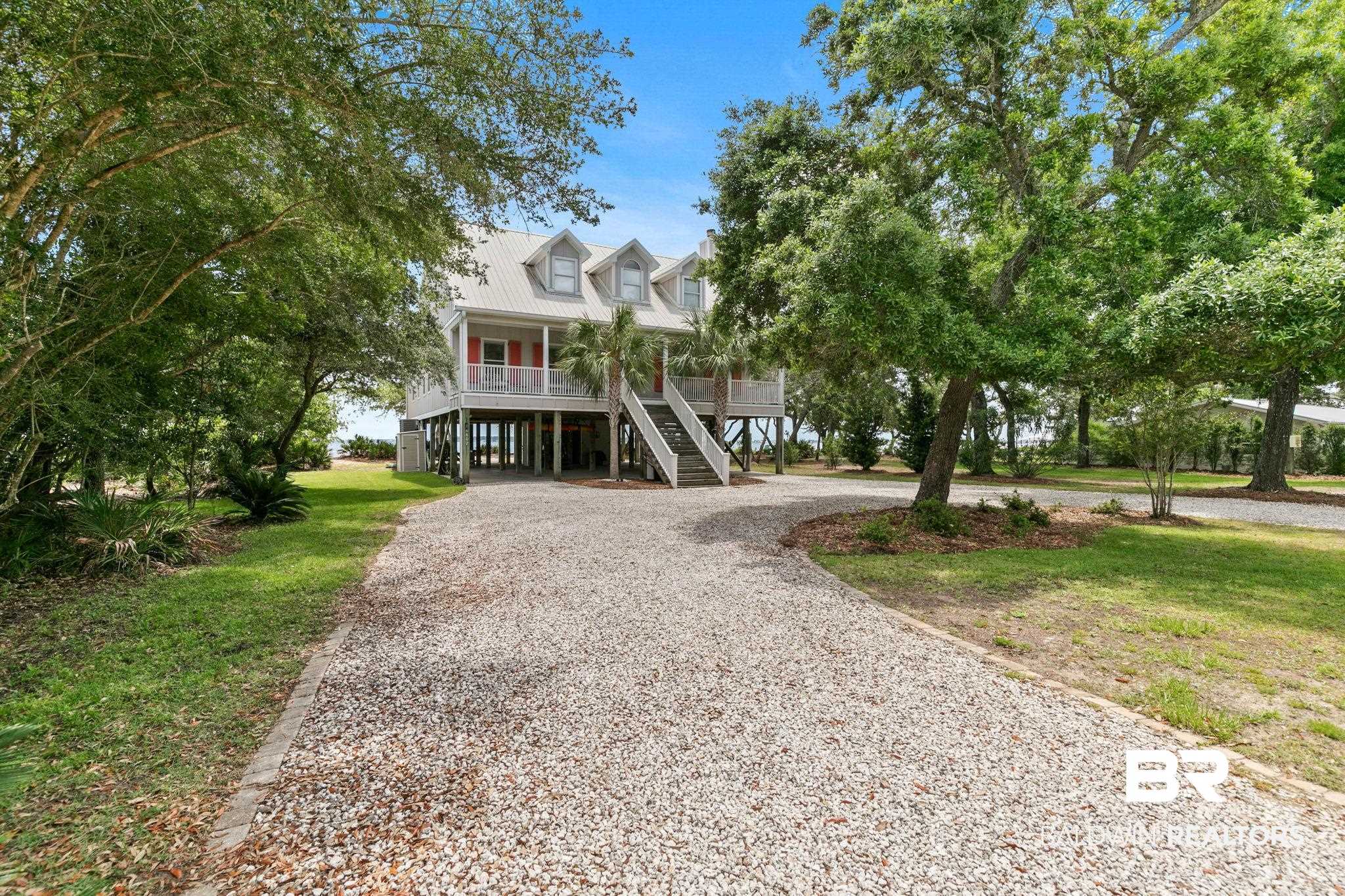 6802 Shore Drive Elberta, AL 36530 - Photo 9 of 34 Elevated coastal residence featuring a wide gravel driveway, mature trees, and a ground-level parking area