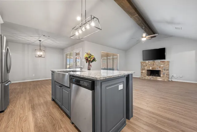 a kitchen with stainless steel appliances granite countertop a refrigerator a sink dishwasher a stove and white cabinets with wooden floor