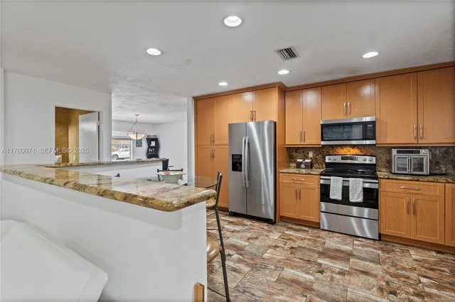 a large kitchen with stainless steel appliances kitchen island granite countertop a refrigerator and a stove top oven
