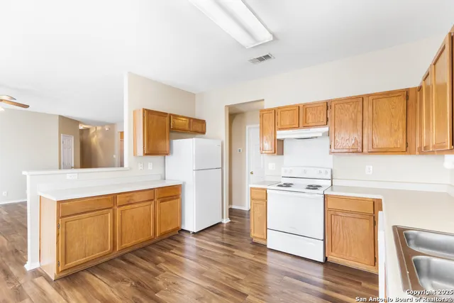 a kitchen with a stove a sink white cabinetry and wooden floors