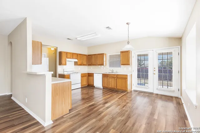 a open kitchen with granite countertop a stove top oven a sink dishwasher and white cabinets with wooden floor