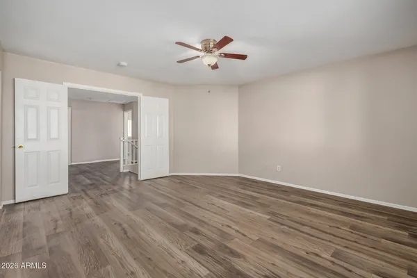 a view of an empty room with wooden floor and a ceiling fan