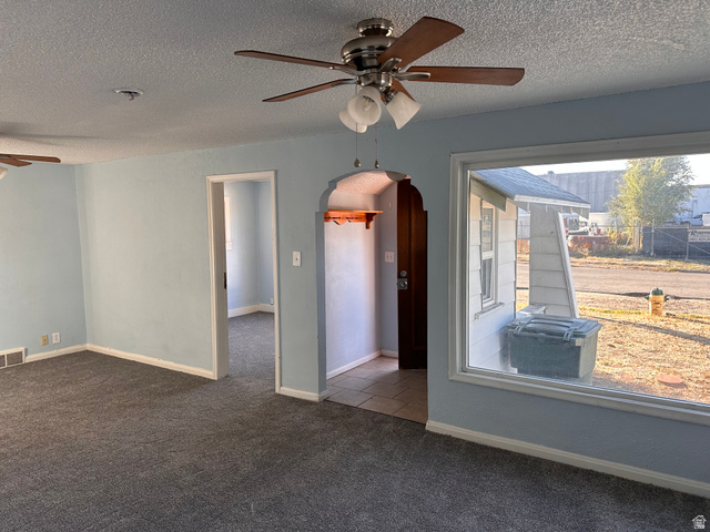 154 East Harris Street Ogden, UT 84401 - Photo 7 of 10 Spare room featuring ceiling fan, a textured ceiling, arched walkways, and dark colored carpet