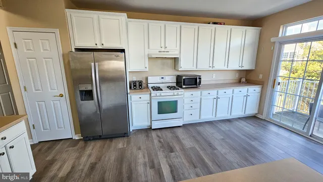 a kitchen with stainless steel appliances granite countertop a refrigerator a sink dishwasher and white cabinets with wooden floor