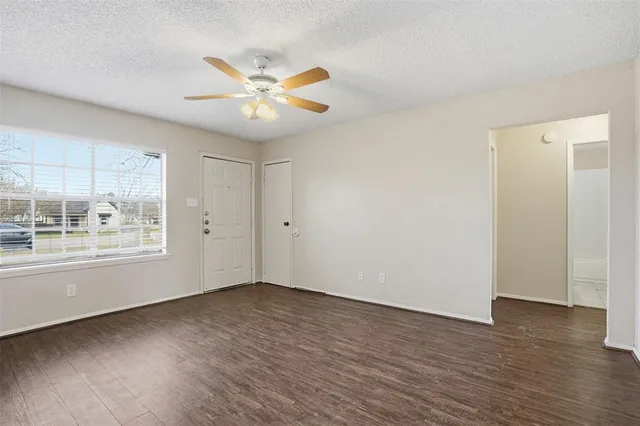 an empty room with wooden floor fan and windows