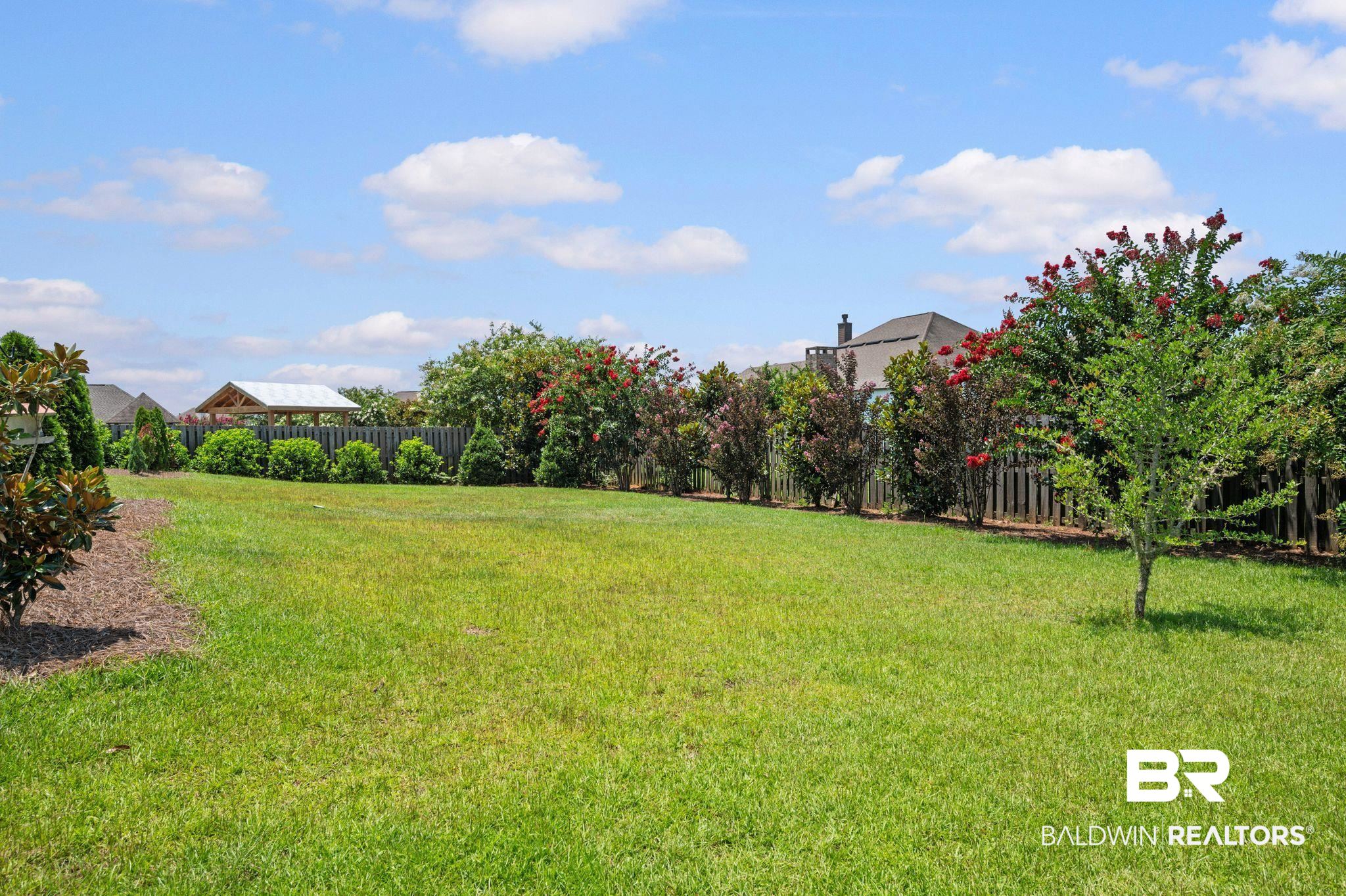 409 Fortune Drive Fairhope, AL 36532 - Photo 41 of 42 Expansive lawn area featuring a wooden privacy fence, mature trees, flowering shrubs, and a built-in outdoor structure