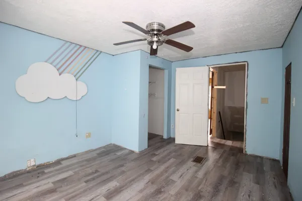 a view of an empty room with wooden floor and a ceiling fan