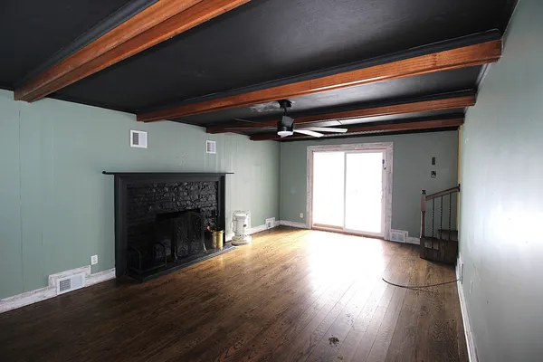 a view of an empty room with wooden floor a fireplace and a window