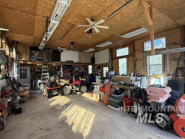 140 Brownlee Loop Road Horseshoe Bend, ID 83629 - Photo 11 of 29 Spacious garage featuring a concrete floor, exposed plywood walls and ceiling, multiple windows providing natural light, and overhead fluorescent lighting with an additional ceiling fan