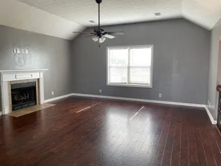 a view of an empty room with wooden floor fireplace and a window