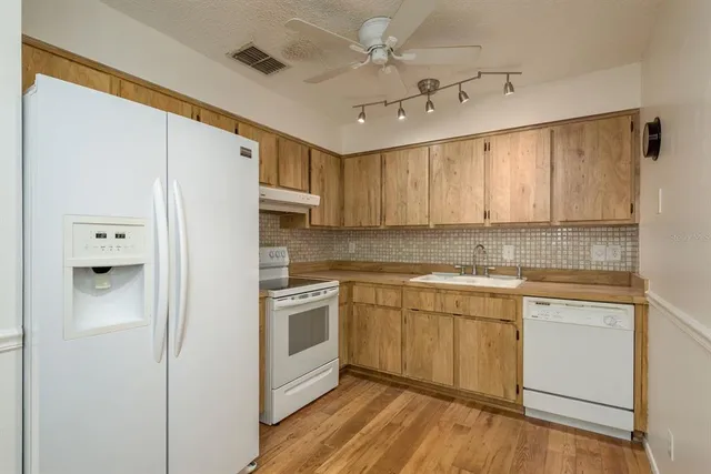 a kitchen with stainless steel appliances granite countertop a refrigerator a sink dishwasher a stove and white countertops with wooden floor