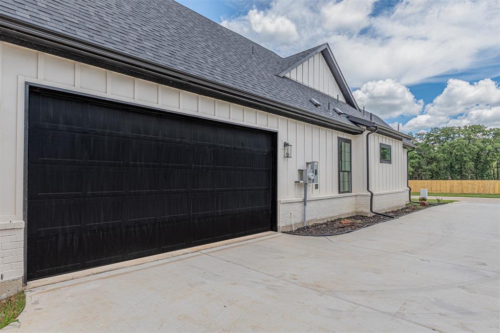 360 Dalton Road Canton, TX 75103 - Photo 28 of 33 Black panel garage door with a concrete driveway, white board-and-batten siding, dark shingle roofing, and black gutters