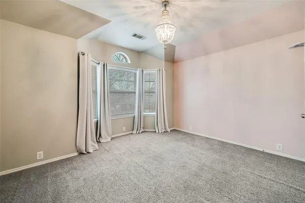 an empty room with chandelier front door and windows